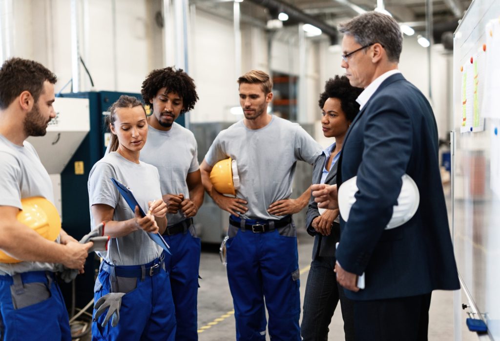 Group of workers having a meeting with company managers in a factory. Focus is on female worker is presenting development reports.